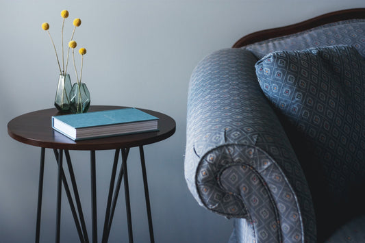 Blue printed antique-style couch next to a side table with book and orange pouf flowers in a vase